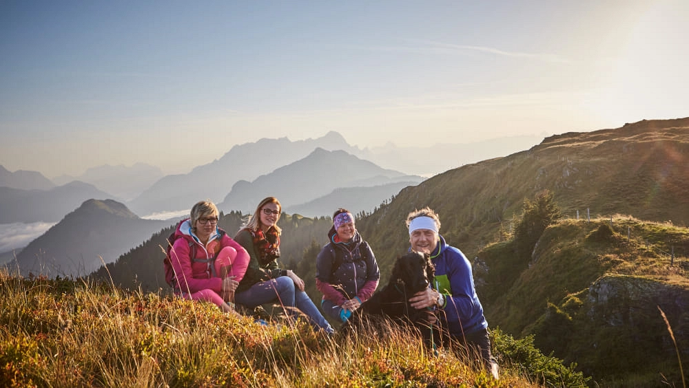 Vier Personen posieren auf einer Bergwiese mit Blick auf die Berge.